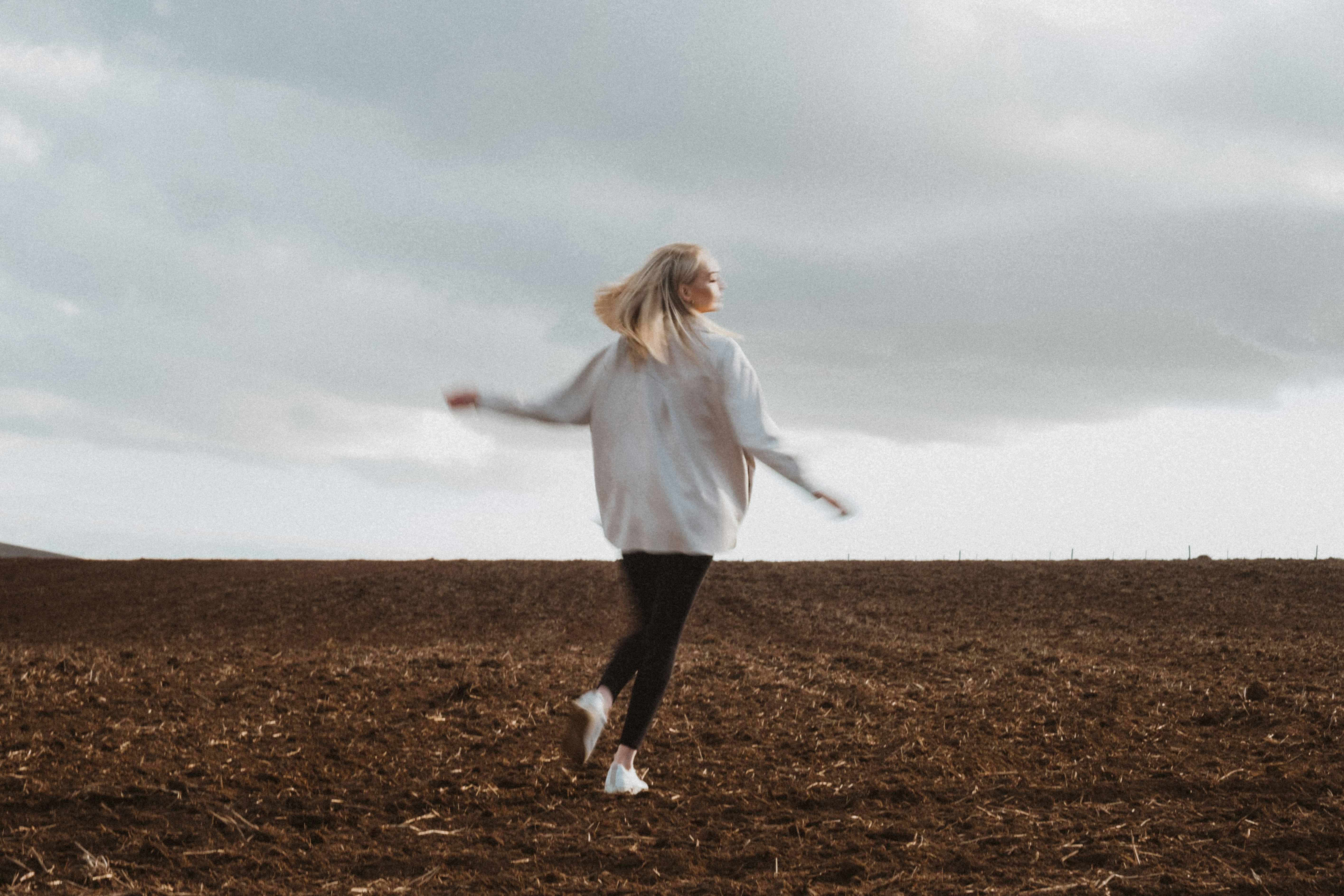 woman in white long sleeve shirt and black pants standing on brown grass field during daytime